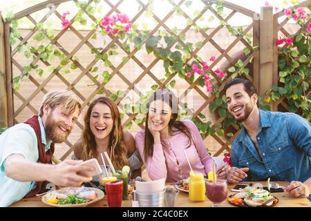Happy friends taking selfie with mobile smartphone while lunching in coffee brunch restaurant - Young trendy people having fun eating together Stock Photo
