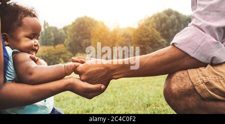 Happy African family having fun together in public park - Black father and mother holding hand with their daughter