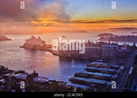 Fog and clouds at sunrise covering sun over major Sydney city landmarks of Circular Quay waterfront of Sydney Harbour. Stock Photo