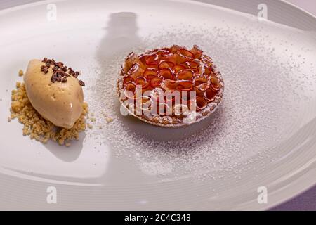 A gourmet dessert of a small apple tart with roses of thin red-skinned apple slices and a quenelle of light brown ice cream with dark shards (possibly cocoa nibs) on crumble lies on a white plate dusted with icing sugar at the Riedel Tasting & Lunch in the Hotel and Restaurant Kronenschlösschen in Hattenheim, Eltville am Rhein, Hesse, Germany. The Riedel Tasting & Lunch on 8 March 2017 is part of the 21st Rheingau Gourmet & Wein Festival. After the glass tasting, Michelin-starred chef Simon Stirnal (Kronenschlösschen) serves a three-course menu. Christian Kraus, managing director of Riedel Gla Stock Photo