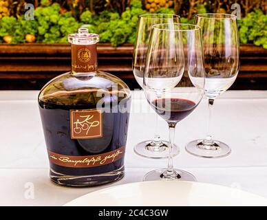 A decanter of "KP – Kirsche im Portweinstil" (port-style cherry) from the Manufaktur Jörg Geiger stands next to a glass with a dark red drink in front of two empty wine glasses on a table with a white cloth in the Hotel and Restaurant Kronenschlösschen in Hattenheim, Eltville am Rhein, Hesse, Germany. The label shows the monogram "KP" with two cherries and the words "im Banyulsfaß gereift" (matured in a Banyuls cask). KP is a partially fermented cherry wine with cherry brandy, matured in casks of Banyuls, a sweet wine from southern France. The decanter is part of the tasting and lunch "Schwäbi Stock Photo