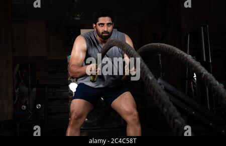 Asian Indian man Doing exercise with Battle rope in Gym Stock Photo