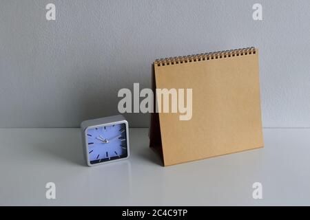 Blank golden spiral binding desk calendar next to a clock placed on white wooden table Stock Photo