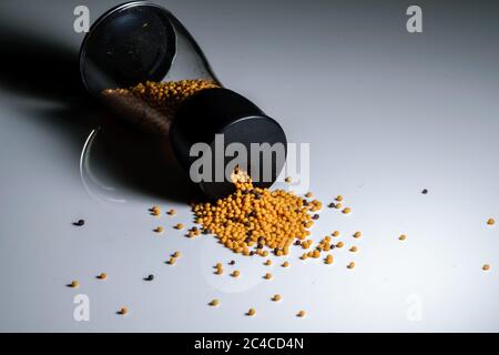 Yellow mustard seeds being poured from a transparent container in a white background Stock Photo