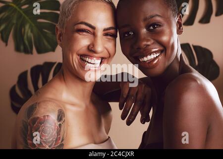 Happy female models looking at camera against leaves in background. Two multi-ethnic women standing together and smiling. Stock Photo