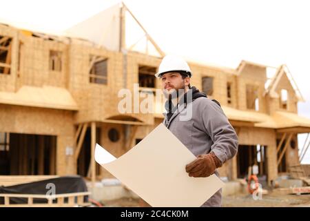 Engineer holding architecture drawing plan on paper at construction site. Stock Photo