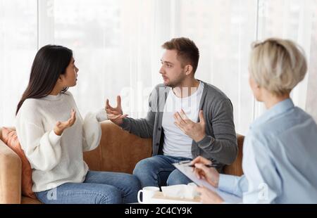 Married Couple Having Quarrel Sitting During Psychologist's Appointment In Office