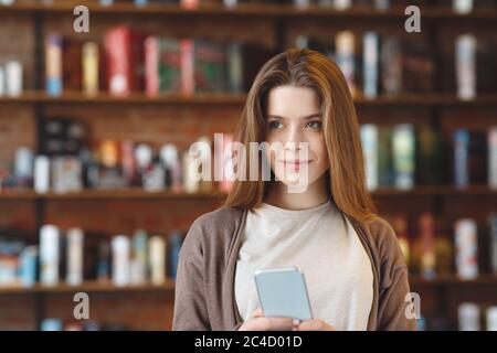 Thoughtful smiling girl looking aside and holding cellphone in hands Stock Photo