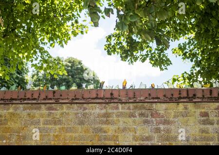 Broken glass bottles cemented to the top of a brick wall, helping to create a deterrent from people climbing the wall. Stock Photo