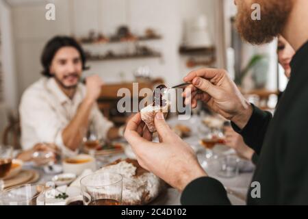 Close up man hands holding slice of bread and spoon in cafe. Group of young international friends spending time together on lunch Stock Photo