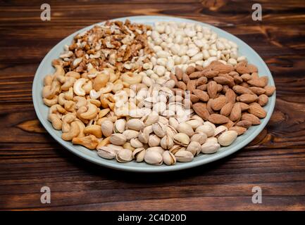 Set of various nuts in plate on wooden background. Healthy food Stock Photo