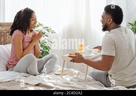 Happy african woman surprised with breakfast in bed Stock Photo