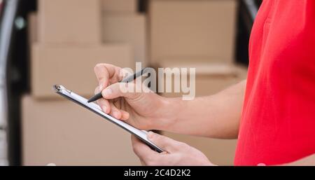 Accurate delivery. Courier notes to tablet delivered parcel, close up, a lot of boxes in car nearby Stock Photo