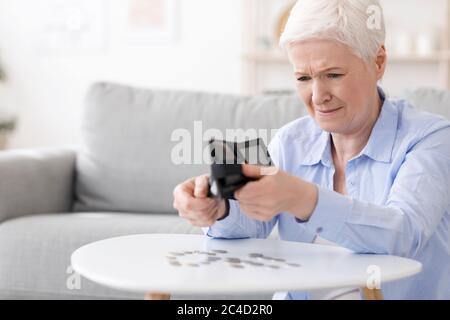 Poverty after retirement. Desperate senior woman shaking out last coins from wallet Stock Photo