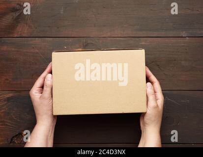 two hands holding a rectangular cardboard box of brown kraft paper over a wooden table, top view Stock Photo