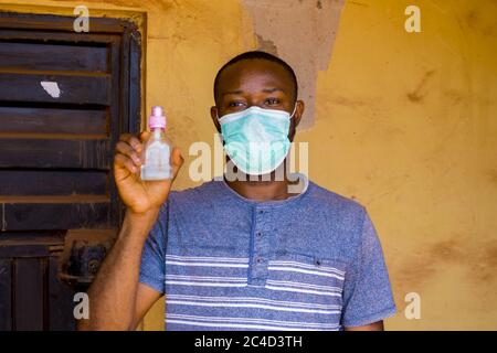 Young African male wearing a surgical mask lifting a mini alcohol on a yellow background Stock Photo