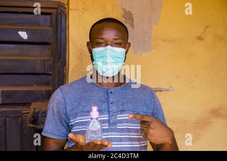 Young African male wearing a surgical mask lifting a mini alcohol on a yellow background Stock Photo