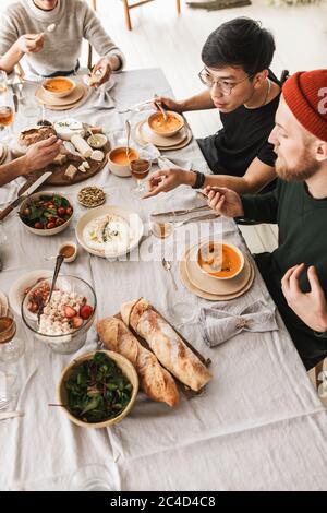 Top view of attractive group of international friends sitting at the table full of food eating together. Young colleagues having lunch spending time Stock Photo