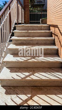 White marble staircase of an Italian house, with white and brown iron railing. Orange brick wall. Stock Photo