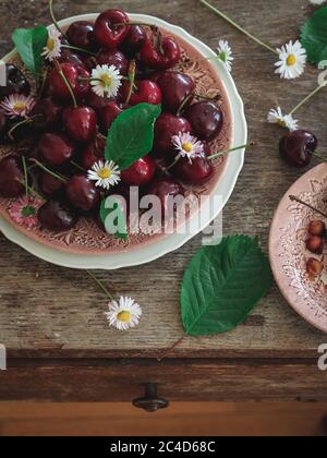Sweet cherries with wild daisies on a plate on a rustic table, shot from above Stock Photo