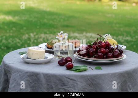 Dessert table setting in a garden with a bowl of sweet cherries and some cream desserts Stock Photo