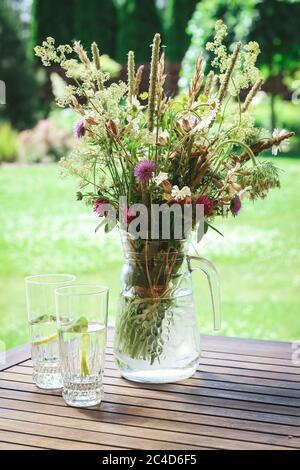 Wildflowers in vase and glasses with water on a terrace table Stock Photo