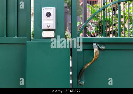 an intercom with a video camera and a microphone for voice communication with a card reader for access by a key card is installed on a green iron gate Stock Photo