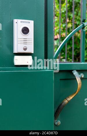an intercom with a video camera and a microphone for voice communication with a card reader for access by a key card is installed on a green iron gate Stock Photo