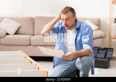 Shocked Man Looking At Shelf Installation Instruction Scratching Head Indoors Stock Photo