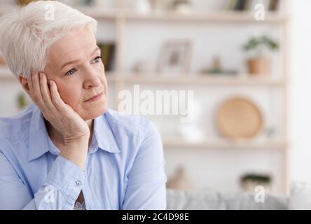 Portrait Of Sad Pensive Senior Woman Sitting At Home And Looking Away Stock Photo
