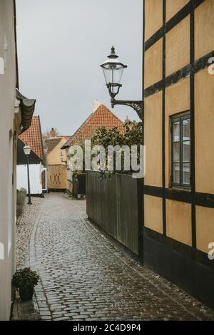 Detail of the street lamp with ornaments hanging on the yellow wall of the old house in the empty street of the oldest Denmark village Ribe Stock Photo