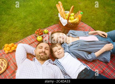 Loving family with adorable boy relaxing under sun during picnic in countryside, view from above Stock Photo