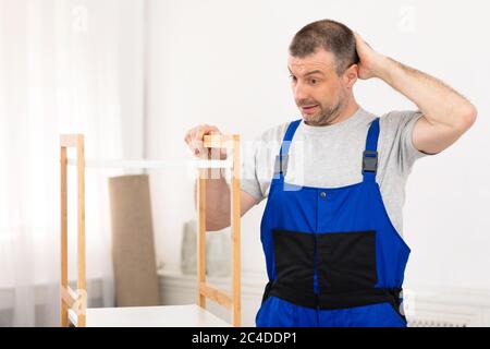 Puzzled Repairman Scratching Head Assembling Cabinet Standing Indoors Stock Photo