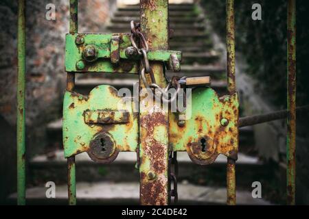 exterior view of a really old, closed and rusty green iron gate with chain and padlock Stock Photo