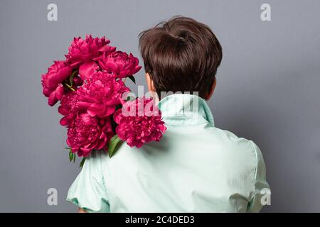 Burgundy red peonies holds woman turned her back on a gray background. Holiday concept. Stock Photo