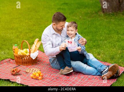 Happy family times. Dad with greeting card and his adorable little boy celebrating father's day on picnic outside Stock Photo