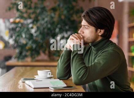 Pensive man sitting alone at cafe, drinking coffee Stock Photo