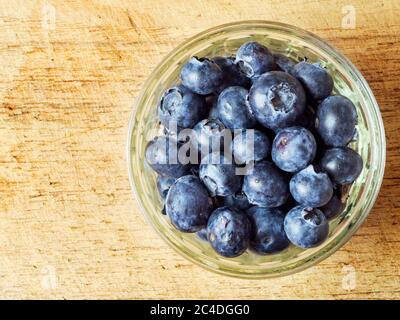 Fresh blueberries in a glass ramekin dish on a wooden chopping board with copy space