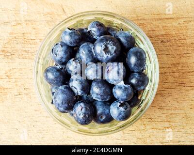 Fresh blueberries in a glass ramekin dish centred on a wooden chopping board