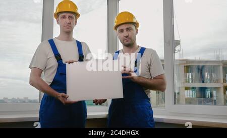 Two sad builders with boardsheet or poster looking for a job. Stock Photo
