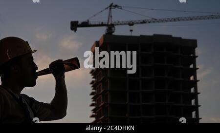 Drunk worker in yellow helmet at construction site. Stock Photo