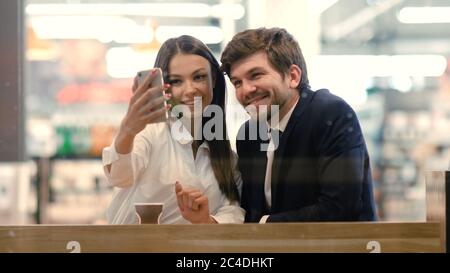Happy young formaly dressed couple using cell phones and taking Stock Photo