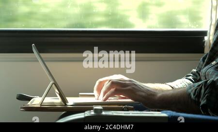 Man hands typing on laptop tablet computer in a train. Stock Photo
