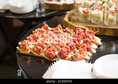 Many sandwiches with jamon and sauce on dark wooden table. Lot of bruschettas with ham or parma. Snack baguette with meat. Catering food concept Stock Photo
