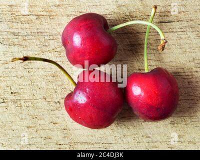 Three fresh ripe cherries on a wooden chopping board Stock Photo