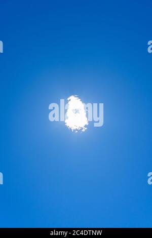 Cloud directly covering the sun and sunlight in a clean blue sky. Centered concept, solitude, unique, sunlight, blue color, tranquility, peace. Stock Photo