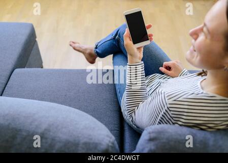 Woman using mobile phone on couch. Smiling, having fun Stock Photo