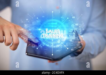 Businessman holding a foldable smartphone with SALES TRAINING inscription, new business concept