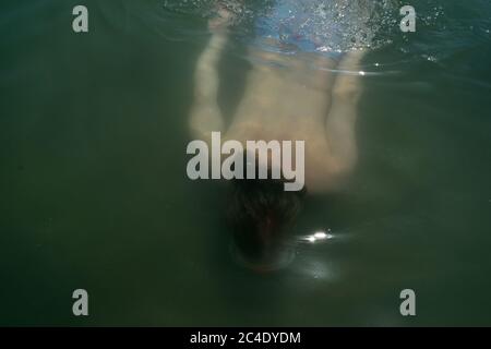 Young Man with Long Blonde Hair Swimming Underwater Stock Photo