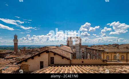 Elevated view of Siena's terracotta rooftops with the Facciatone and Torre del Mangia in the distance. Tuscany, Italy.